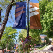 Two Westminster College banners, copper and dark purple, and a flower basket hang from a light post in Richer Commons.
