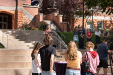 President Beth Dobkin stands behind a lectern on the stairs in front of Converse Hall while contributors to this partnership stand beside her to the right.